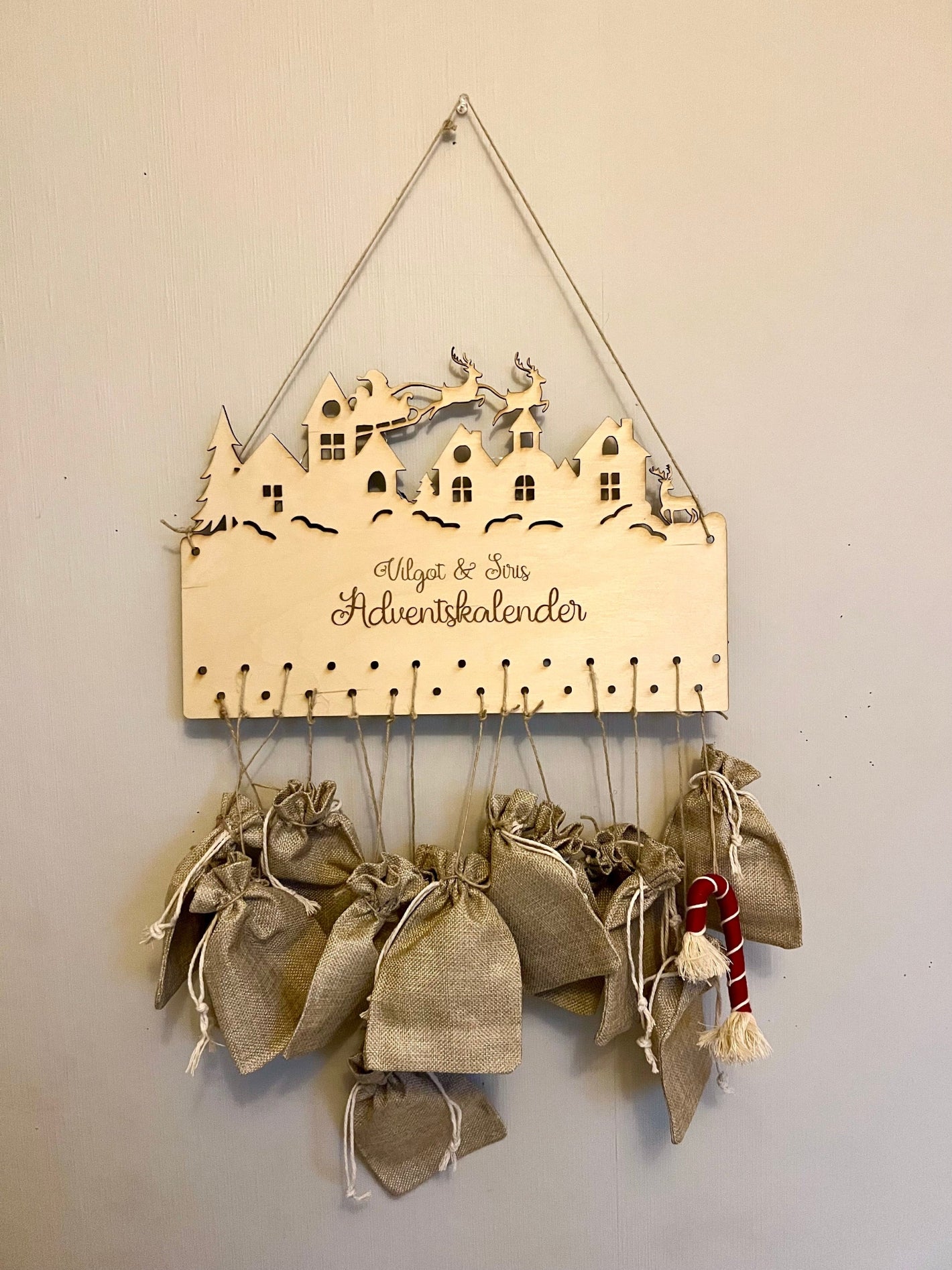 Personalized wooden advent calendar made from birch plywood, engraved with name and city skyline design featuring Santa’s sleigh and reindeer.