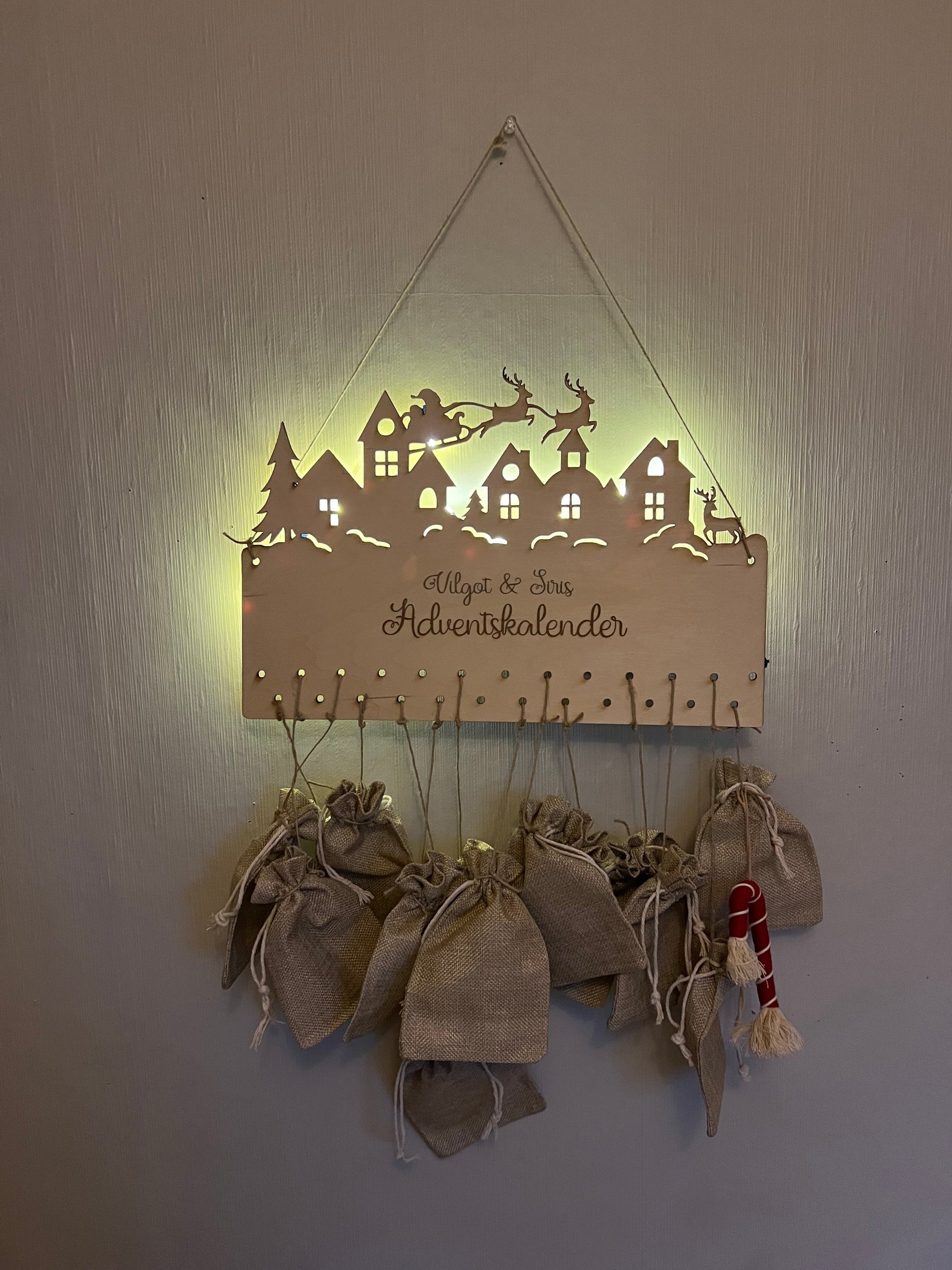 Close-up of a personalized wooden advent calendar made from birch plywood, featuring engraved city skyline, Santa’s sleigh, and 25 holes for hanging small gifts.